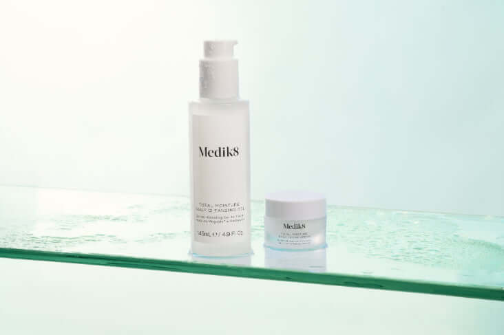 Medik8 Total Moisture Daily Cleansing Gel and moisturizer on a glass surface with water droplets.