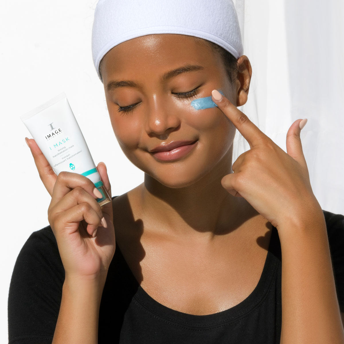 IMAGE Skincare I MASK Firming Transformation Mask applied to the cheek by a model