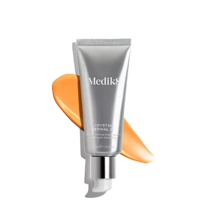Medik8 Crystal Retinal 24™ serum in a silver tube with orange cream swatch behind it