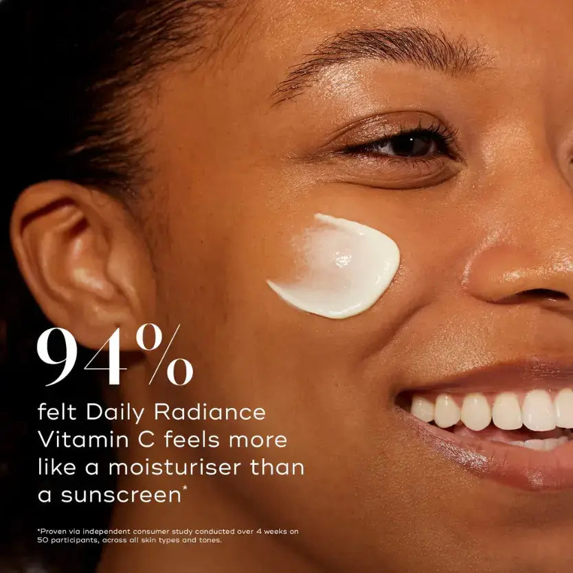 A smiling person applying Medik8 Daily Radiance Vitamin C™ on their cheek, showcasing the cream's texture.