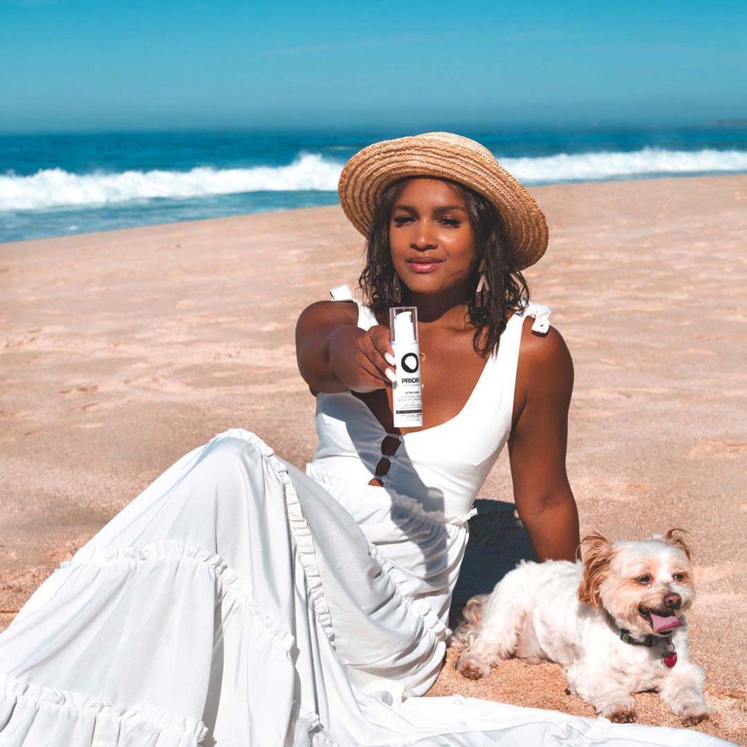 PRIORI Tetra Tinted Day Shield held by a model on the beach
