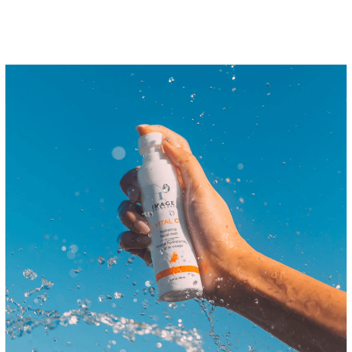 IMAGE Skincare VITAL C Hydrating Facial Mist held in hand with water splashes against a blue sky